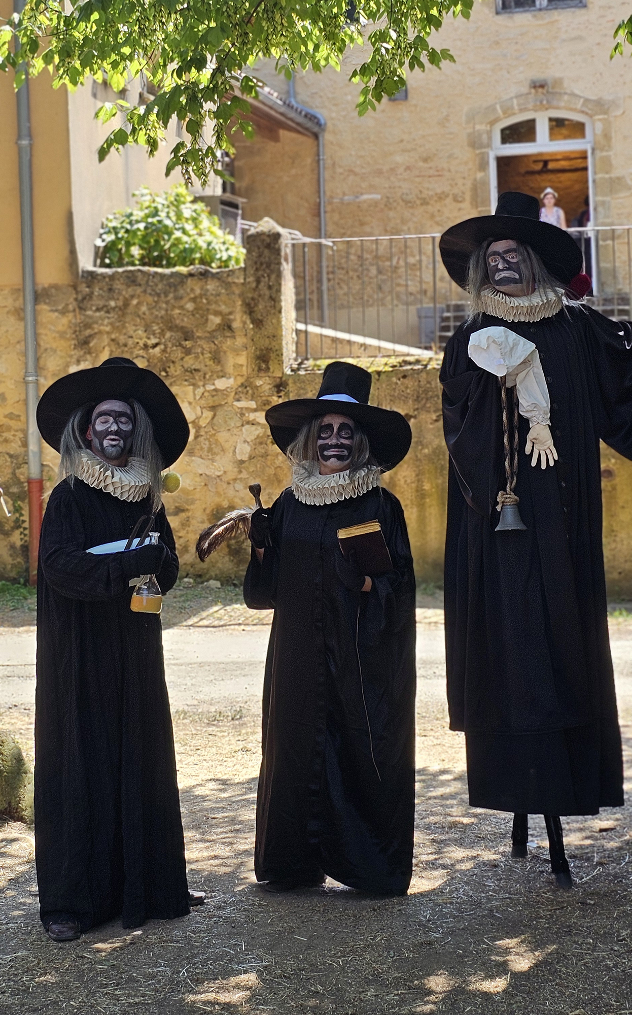 Trois comédiens costumés avec de longues robes noires et des chapeaux noirs.