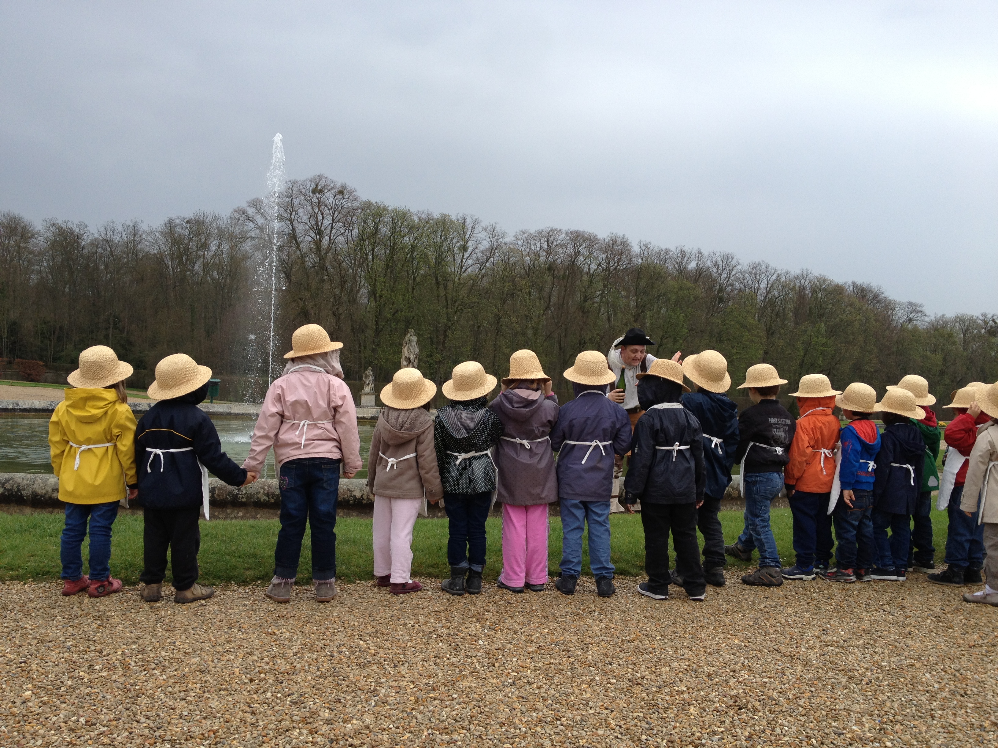 Groupe d'enfants de dos portant chacun un chapeau et admirant un comédien dans le jardin du Château de Vaux-le-Vicomte.