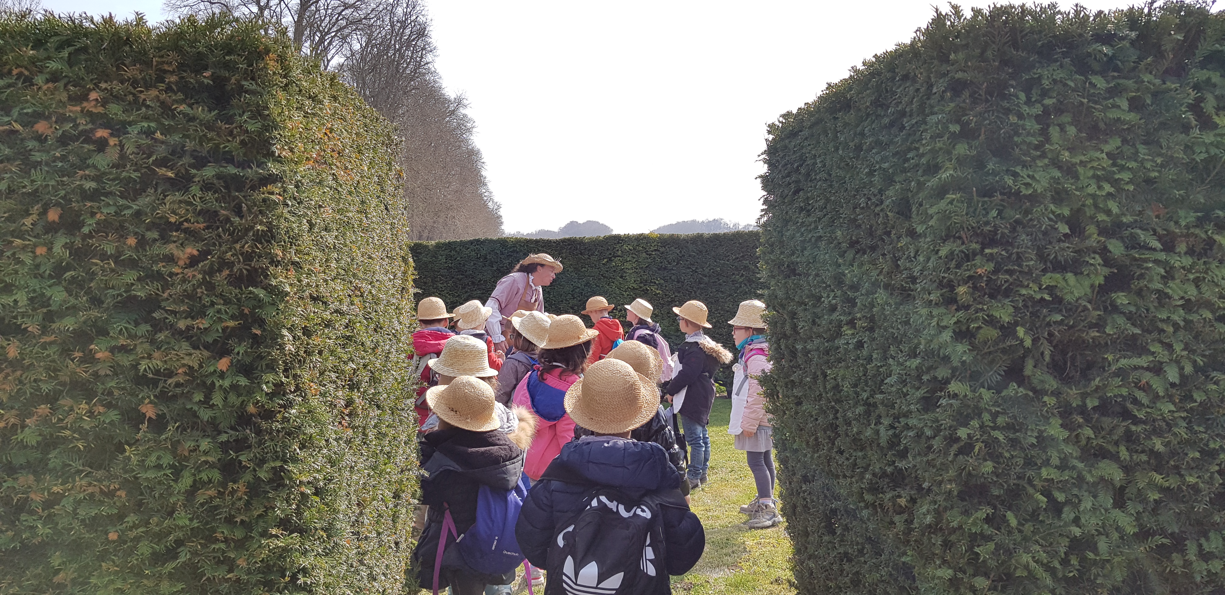 Groupe d'enfants de dos portant chacun un chapeau et admirant un comédien dans le jardin du Château de Vaux-le-Vicomte.