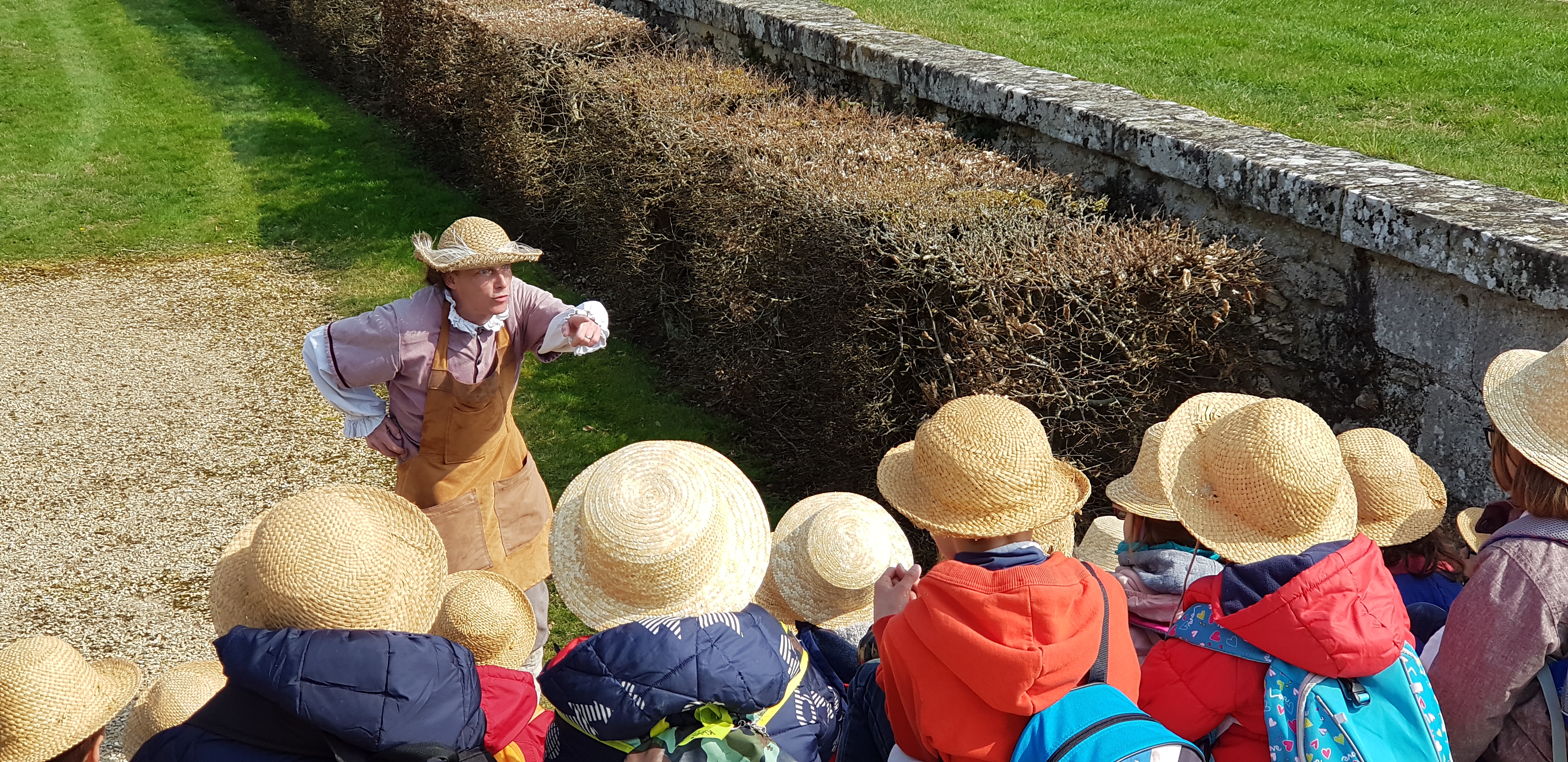Groupe d'enfants de dos portant chacun un chapeau et admirant un comédien dans le jardin du Château de Vaux-le-Vicomte.