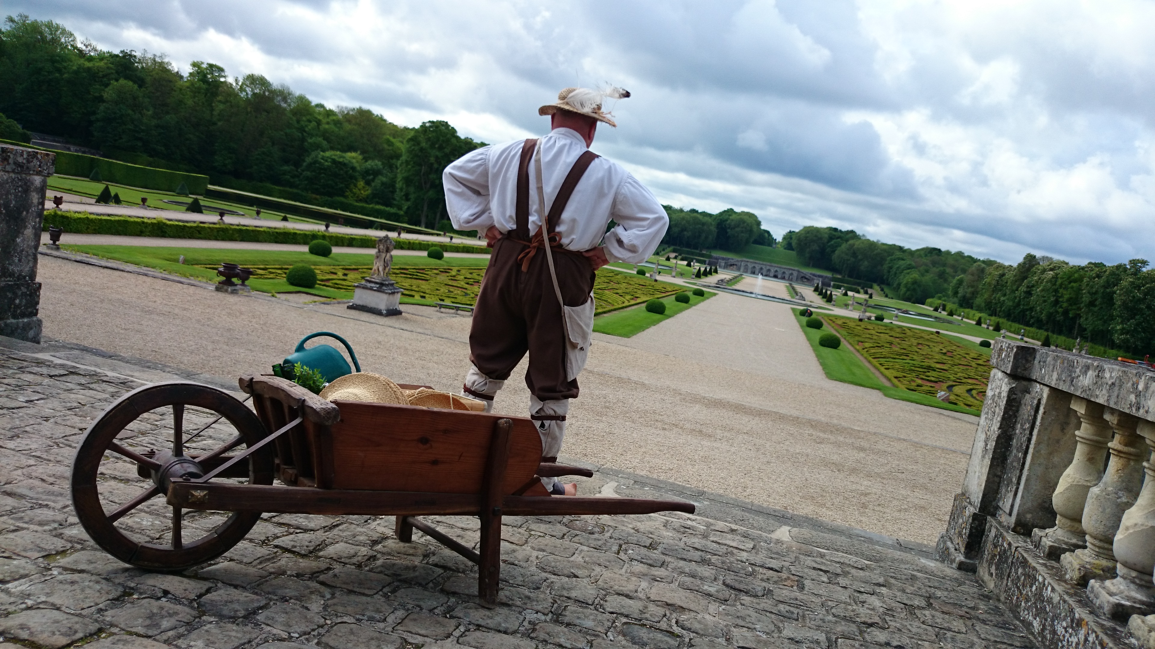 Homme déguisé en "Amédée, le jardinier" de dos regardant le jardin du Château de Vaux-le-Vicomte.