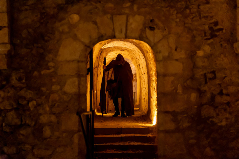 Un comédien s'approchant de l'objectif situé dans l'embrasure d'un couloir de pierres.