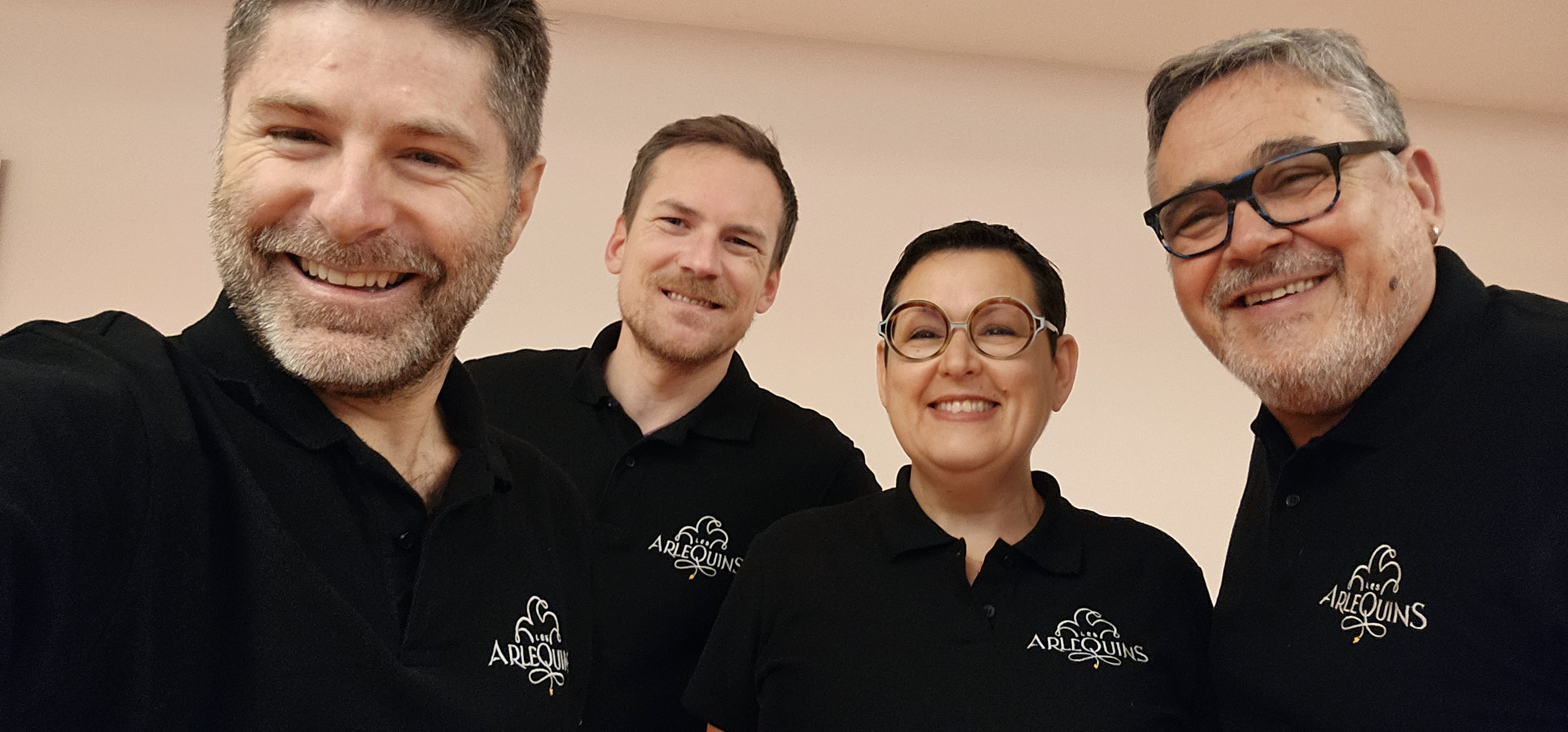 Trois hommes et une femme vêtus d'un polo noir avec le logotype Les Arlequins. La photographie est prise en mode selfie.