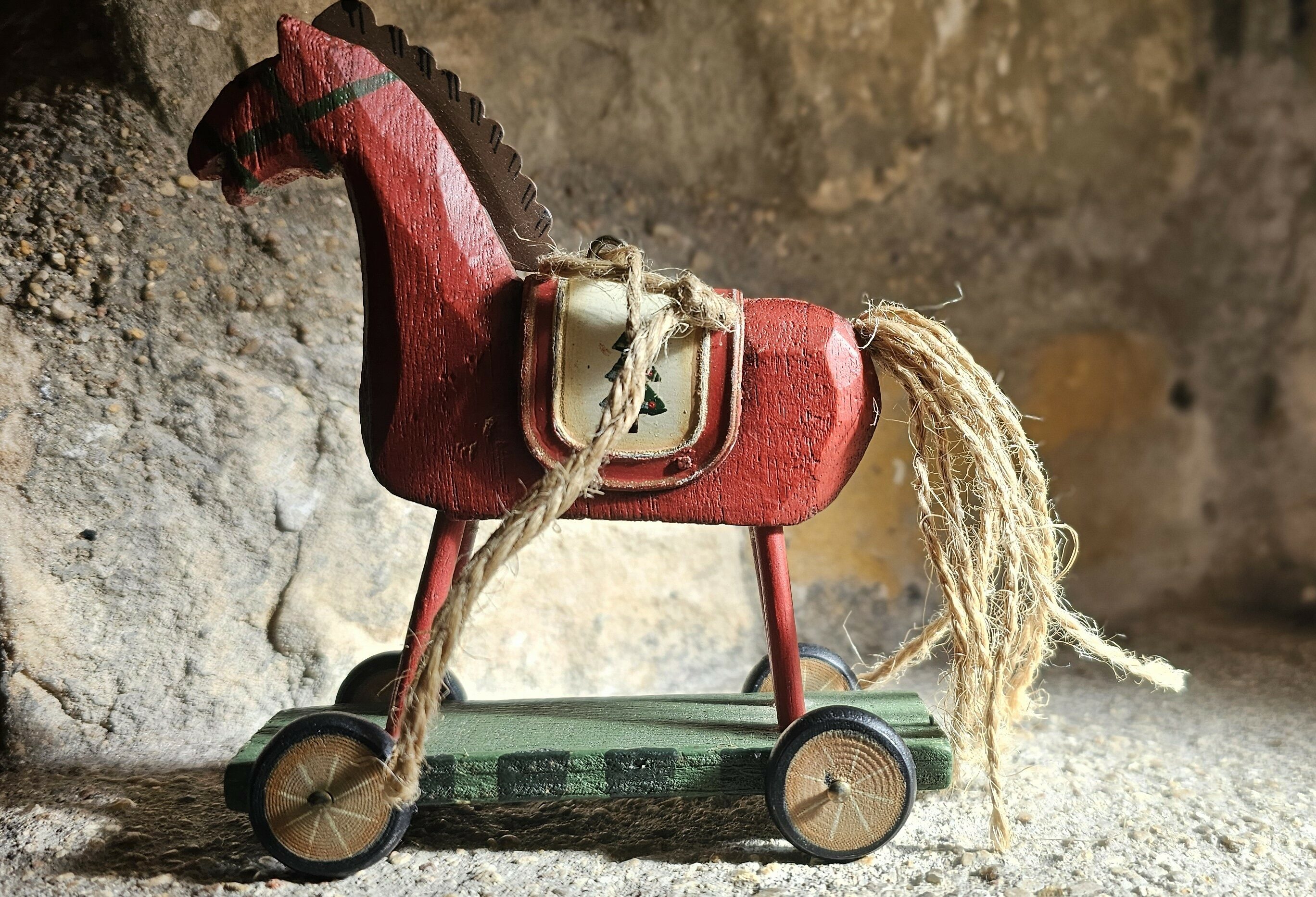 Cheval rouge en bois avec des petites roues posé sur une pierre.