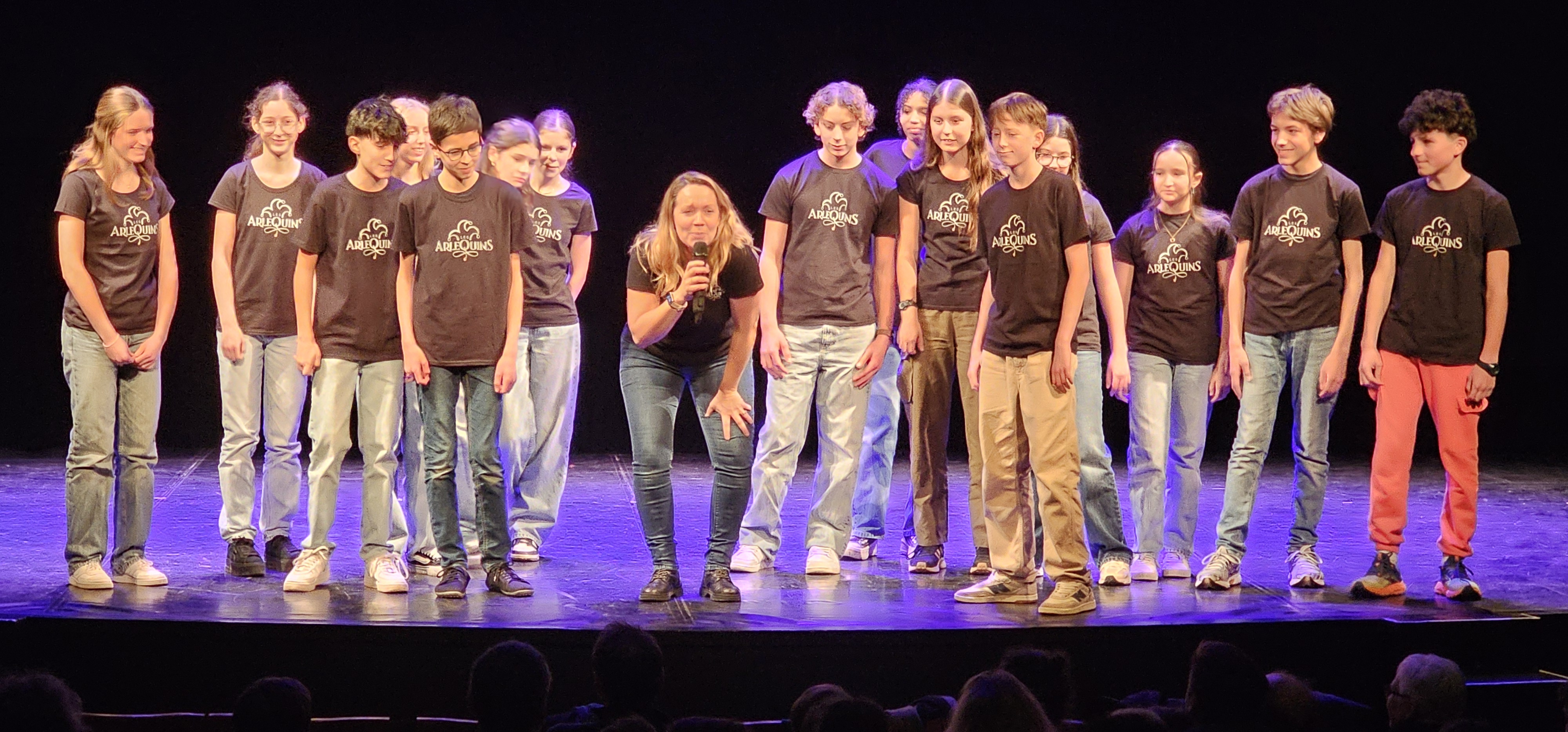 Groupe d'adolescents sur une scène de théâtre face à un public.